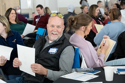 Educators in breakout groups at a conference, one male educator is looking on and smiling