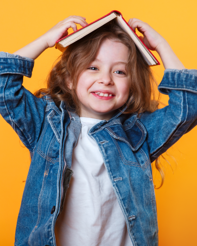 Young child smiling playfully with a book on her head