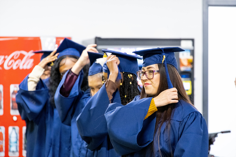 A woman in a blue cap and gown moves her tassel to the left side of the cap.