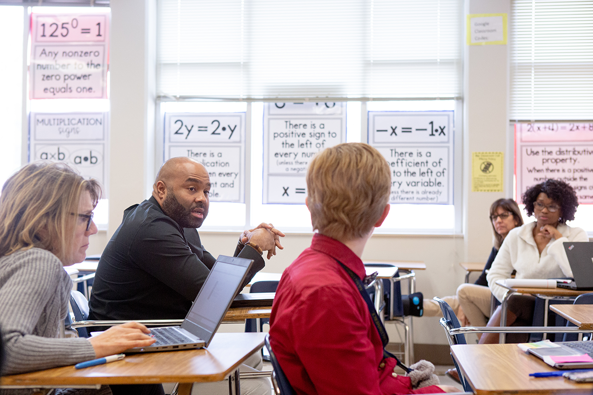 Group of adults in a classroom setting having a discussion, focus is on a man who is speaking